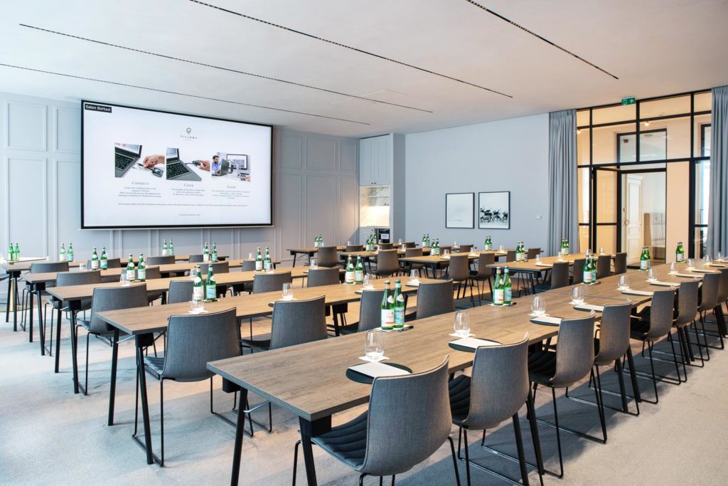 A large meeting room with a grey chairs at long tables